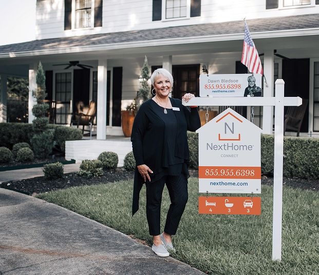 A woman standing next to a NextHome for sale sign